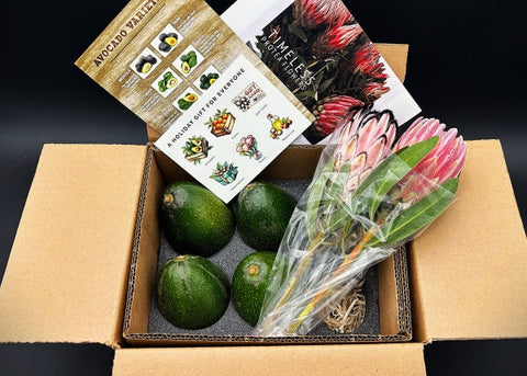 Box containing avocados and a bouquet of flowers with a card on a dark background
