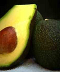 Fresh California avocado sliced open with pit, next to whole avocado on white surface
